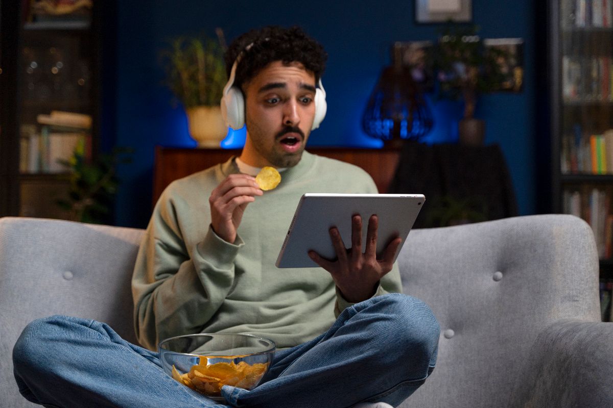 Homme avec casque audio et tablette sur canapé, bouche bée car 15€ offerts sur le streaming avec la Livebox Max